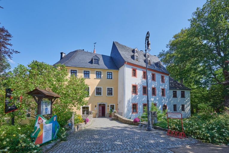 Eine Straße führt zu einem Haus. Dort ist der Eingang zu einem Schloss. Es ist ein kleines Schloss.