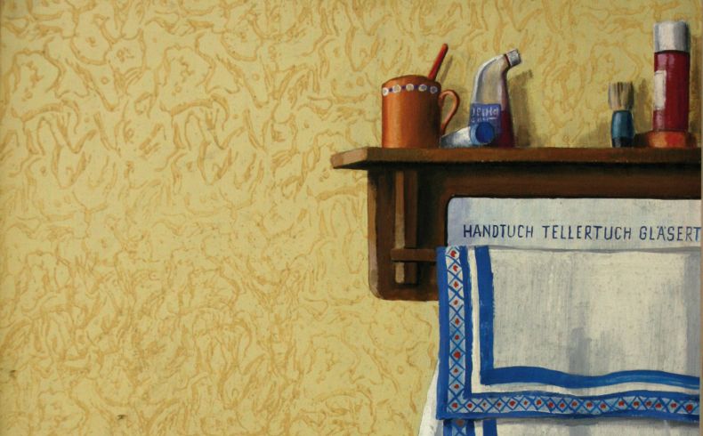 Ausschnittartiges Bild mit einer traditionellen Küchenwand, links ein schwarzer Lichtschalter und ein Abreißkalender, rechts angeschnitten ein Küchenbord mit Utensilien wie Tasse, Rasierpinsel, darunter hängen weiße Geschirrtücher