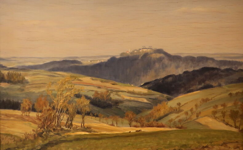 Blick über eine Wiese mit Birken und Sträuchern am Wegrand auf die Augustusburg im Herbst